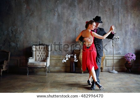 Young pretty woman in red dress and man in black suit dance tango
