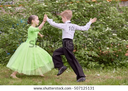 Children couple dances ballroom dance outdoor at grassy lawn.