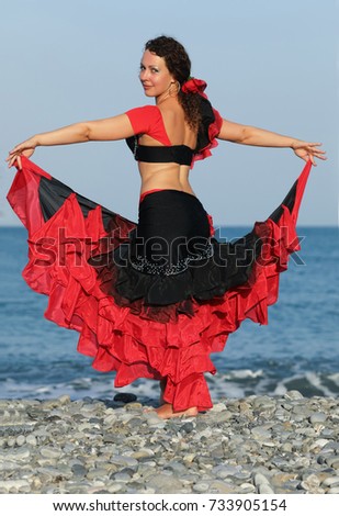 dancer woman in black and red suit dancing on seashore, straightened her skirt