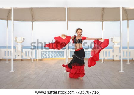 beautiful dancer woman in black and red suit with fan dancing on seashore