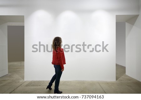 Woman in red looks at white wall in exhibition of art, back view