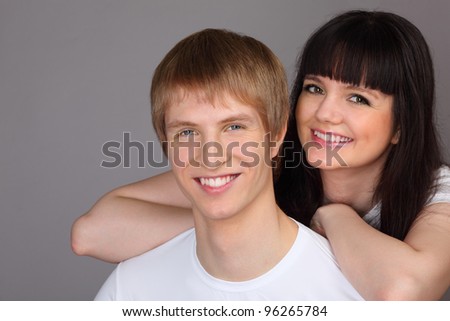 Young happy man and woman dressed in white shirts on gray background; focus on man