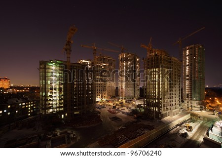 Seven high buildings under construction with cranes and illumination at dark night