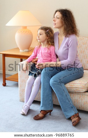 Mother and daughter sits on couch in cozy room, mom says and daughter listens
