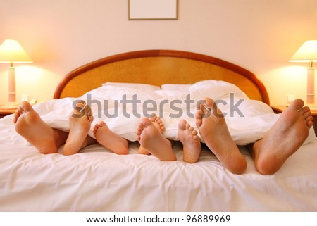 Mother, father and two children lie on bed with white sheets; focus on feet