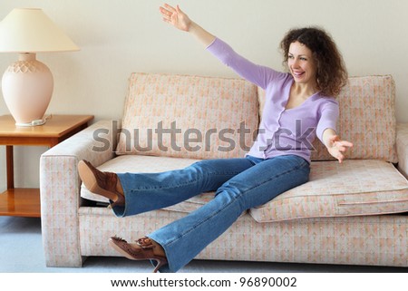 Beautiful laughing woman jumped on couch in simple comfortable room