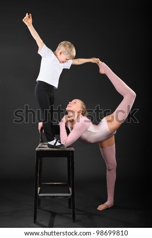 Girl and little boy gymnast took graceful pose at bark chair in black studio