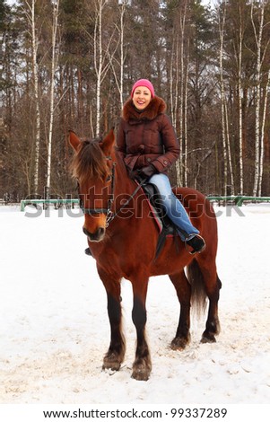 Beautiful young woman sits on brown horse and smiles at winter