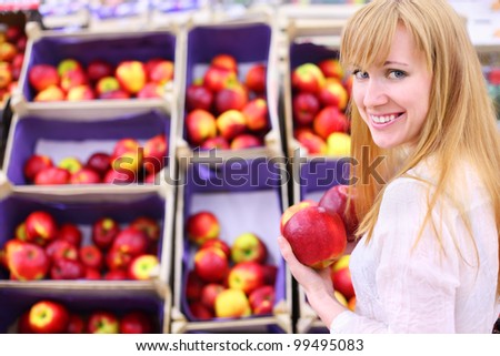 Happy girl wearing white shirt chooses apples in store; shallow depth of field
