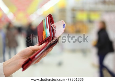 Woman hand keep red purse with money and credit cards in store; shallow depth of field