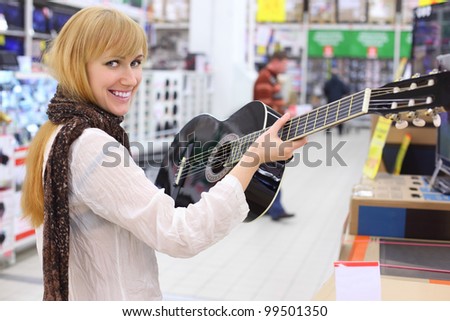 Happy girl wearing scarf holds guitar in supermarket; shallow depth of field