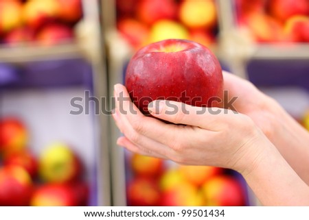 girl hands hold big red apple in shop; shallow depth of field