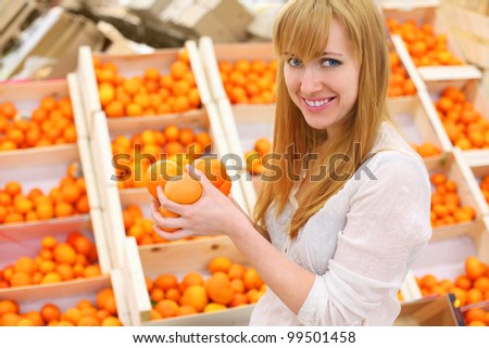 Blonde girl wearing white shirt holds oranges in store; shallow depth of field
