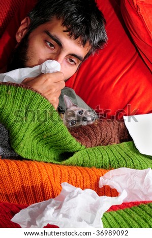 A sick man at home, laying down with his cat and tissue paper.