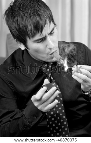 A young successful man lighting up a cigar with a match in his left hand and a matchbox in his right hand.
