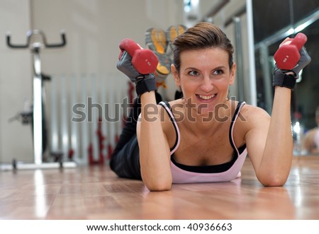 Young woman exercising on her stomach, on a wooden gym floor with dumbells in her hands.