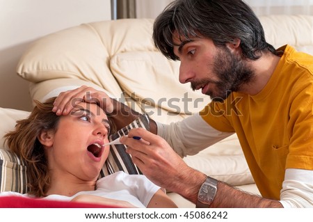 A woman is having her temperature checked by a man while she lays on the sofa.