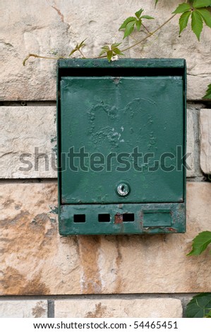 A rustic green mailbox on a stone wall with vines around it.