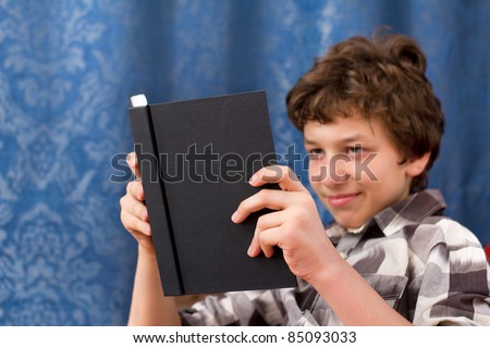 A pre-teen boy reading a black book. The boy is out of focus in the background and the book is in focus in the foreground.