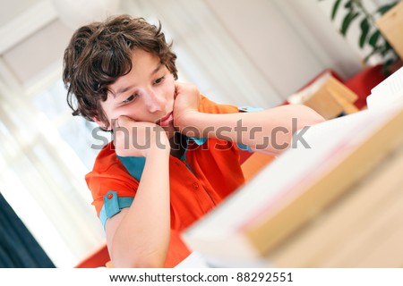 A teen school boy studies hard over his books at home as he props his head up with his arms.