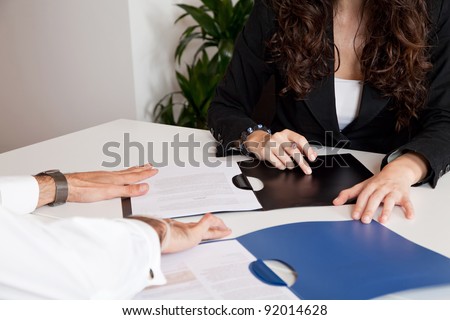 The hands of two business associates, one male and one female, are seen overlooking business files or contracts in plastic folders.