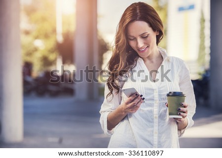 beautiful young woman is using an app in her smartphone device to send a text message in front of a sunset background