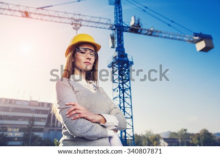 beatiful woman engineer is standing serious in front of a crane