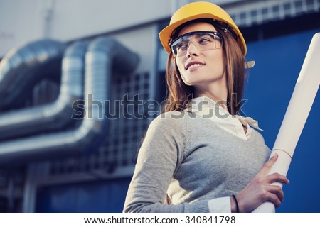 beautiful woman engineer is standing in front of an industrial pipes background