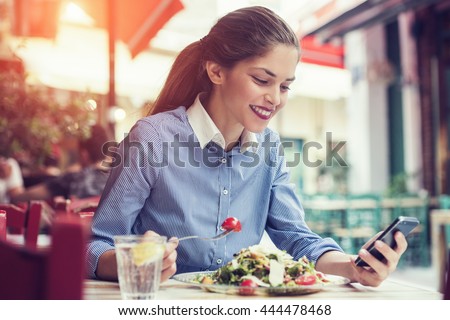 beautiful young woman using an application to send an sms message in her smartphone device while eating a salad