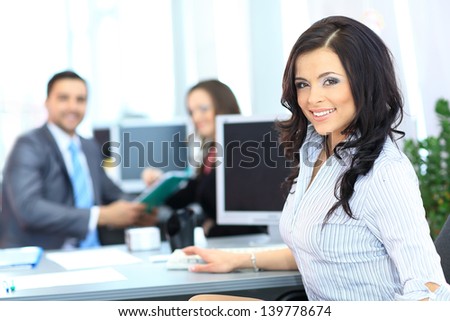 Happy young businesswoman looking behind and her colleagues working at office