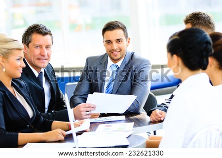 Portrait of young handsome businessman in office with colleagues in the background