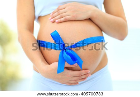 woman holding hands on her baby bump, tied with a blue bow