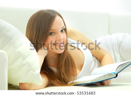 Full length of a young lady lying on sofa reading book