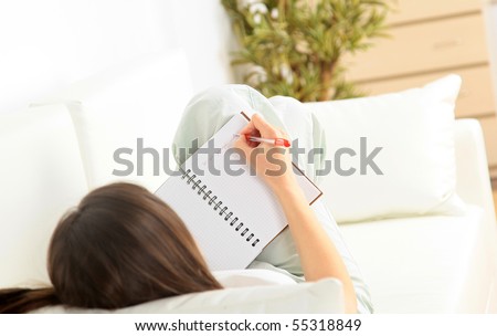 Portrait of a smiling young woman lying on sofa and writing documents