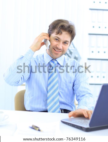 Handsome business guy working on cellphone and laptop together while at work