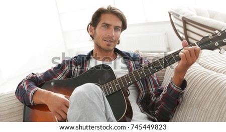 modern guy with guitar sitting on sofa in living room.