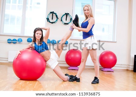 Two smiling women do stretching exercise in sports club. Fitness gym