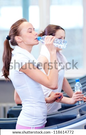 Two young women drinking water after sports. Fitness gym.