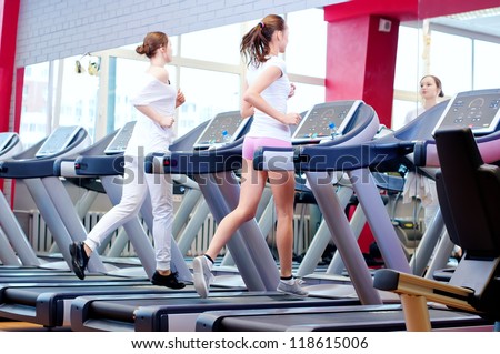 Two young sporty women run on machine in the gym centre