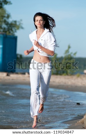 Beautiful young sport woman running on water at sea coast