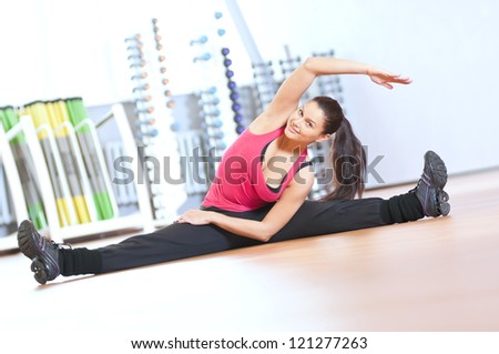 Young fitness woman doing stretching exercises on the floor at the sport gym club