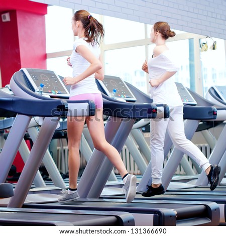 Two young sporty women run on machine in the gym centre - stock photo