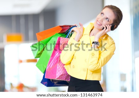 Happy woman with shopping bags in mall center talking by phone. Sales.