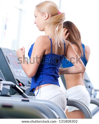 Two young sporty women run on machine in the gym centre