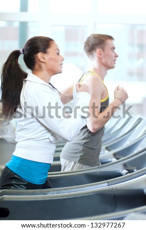 Young woman and man at the gym exercising. Run on a machine.