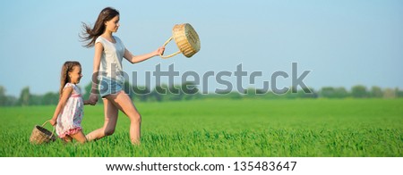Young happy girls running with basket at green wheat field with her friend together