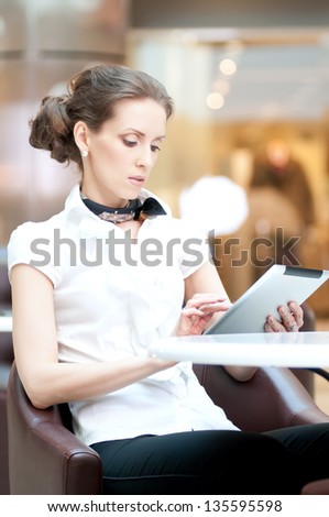Young professional businesswoman sitting at table at cafe and using tablet on lunch break