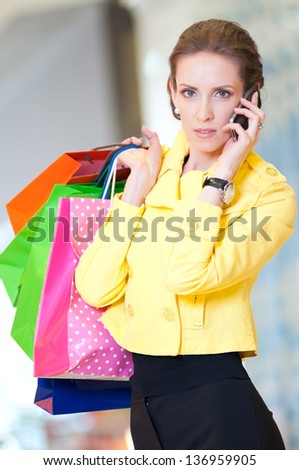 Happy woman with shopping bags in mall center talking by phone. Sales.