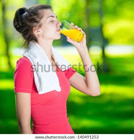 Young woman drinking fresh orange juice after sport fitness exercise at green summer park
