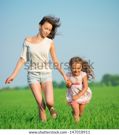 Young happy girls running down green wheat field with her friend together